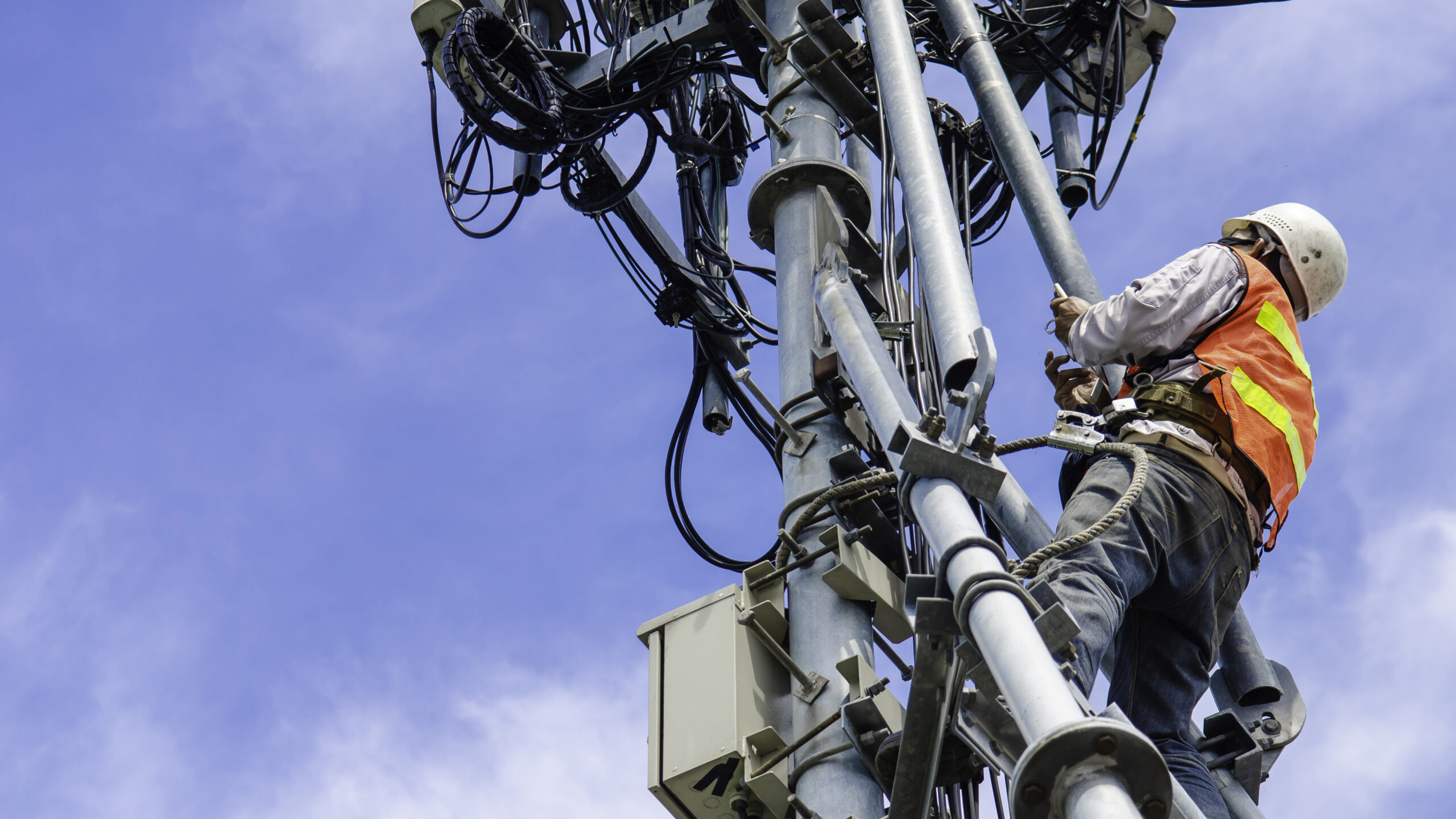 Low Angle View Of Man Working On Communication Tower Against Sky